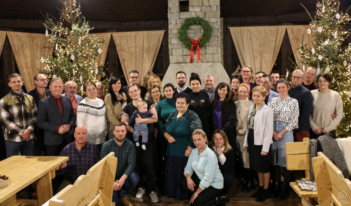 Lokalni producenci we wspólnym zdjęciu, stoją przed choinkami w altanie w skansenie.