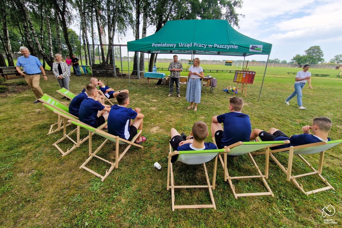 Podopieczni ośrodka siedzą na leżakach, przed nimi pracownicy PUP w Pszczynie.