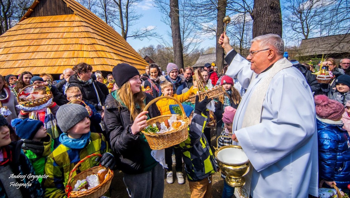 Ksiądz święcący pokarmy w koszyczkach, które trzymają licznie zgromadzeni ludzie.