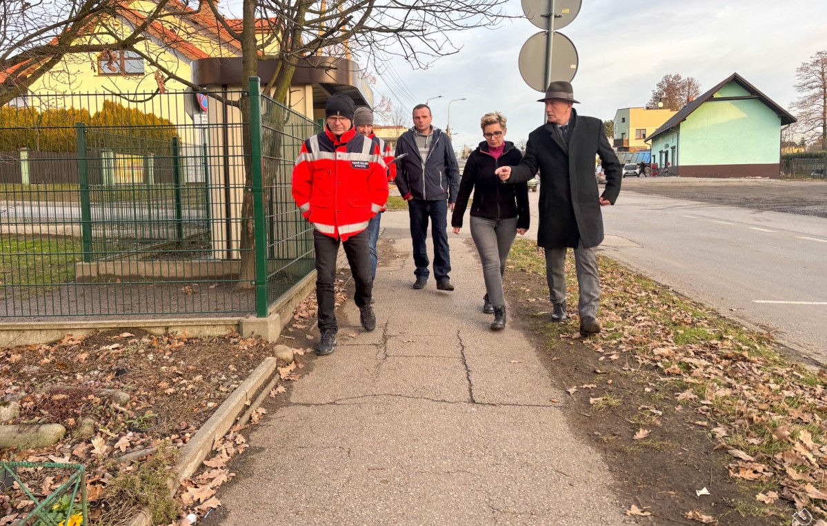 członek zarządu, sołtys Piasku, przedstawiciel zarządu dróg i wykonawcy idą chodnikiem, który ma być wyremontowany