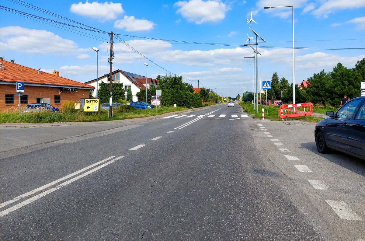 Ulica Pszczyńska w Woli. Nierówna droga z koleinami pomiędzy zabudową.