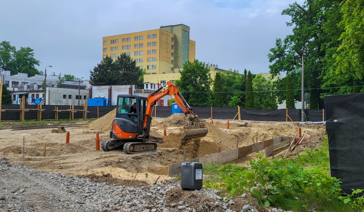 Plac budowy na którym koparka wkypuje ziemię pod fundamenty. Na drugim planie widoczny budnek pszczyńksiego szpitala
