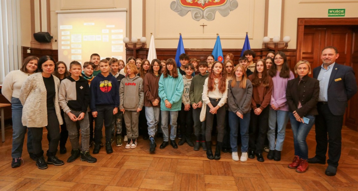 Uczniowie we wspólnym zdjęciu z nauczycielami i uczniami w sali sesyjnej.