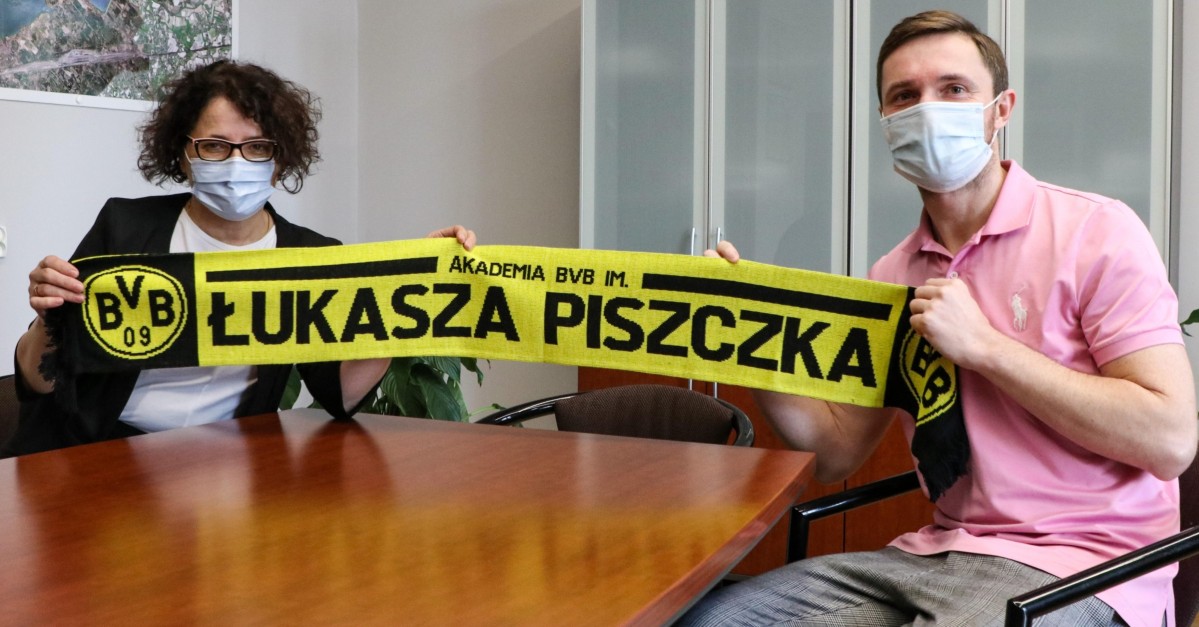 Starosta Barbara Bandoła i Michał Zioło z Akdaemii BVB siedzą przy stole i trzymają szalik z napisem Akademia BVB im. Łukasza Piszczka
