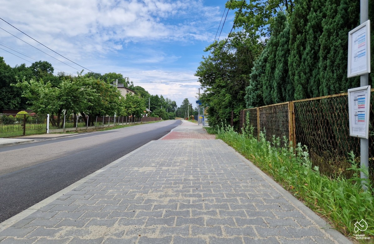 Nowy chodnik z kostki betonowej, obok znak przystanku. W oddali widać zatokę autobusową.