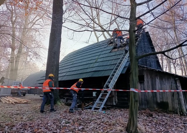 Robotnicy rozbierający dach drewnianego obiektu.