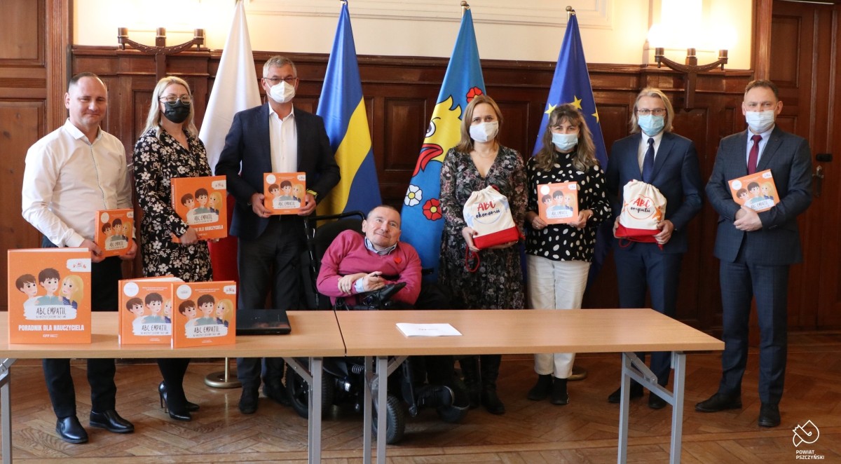 Przedstawiciele samorządów oraz fundacji stoją obok siebie w sali sesyjnej starostwa, trzymając publikację
