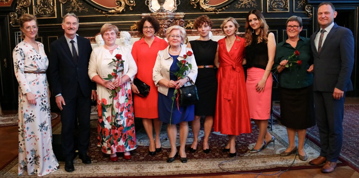 Laureatki odznaczenia Klejnot Ziemi Pszczyńskiej wraz z członkami Zarządu Powiatu Pszczyńskiego stoją obok siebie w sali lustrzanej pszczyńskiego zamku.