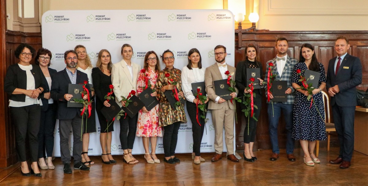 Nauczyciele mianowani i władze powiatu stoją w sali sesyjnej i pozują do zdjęcia