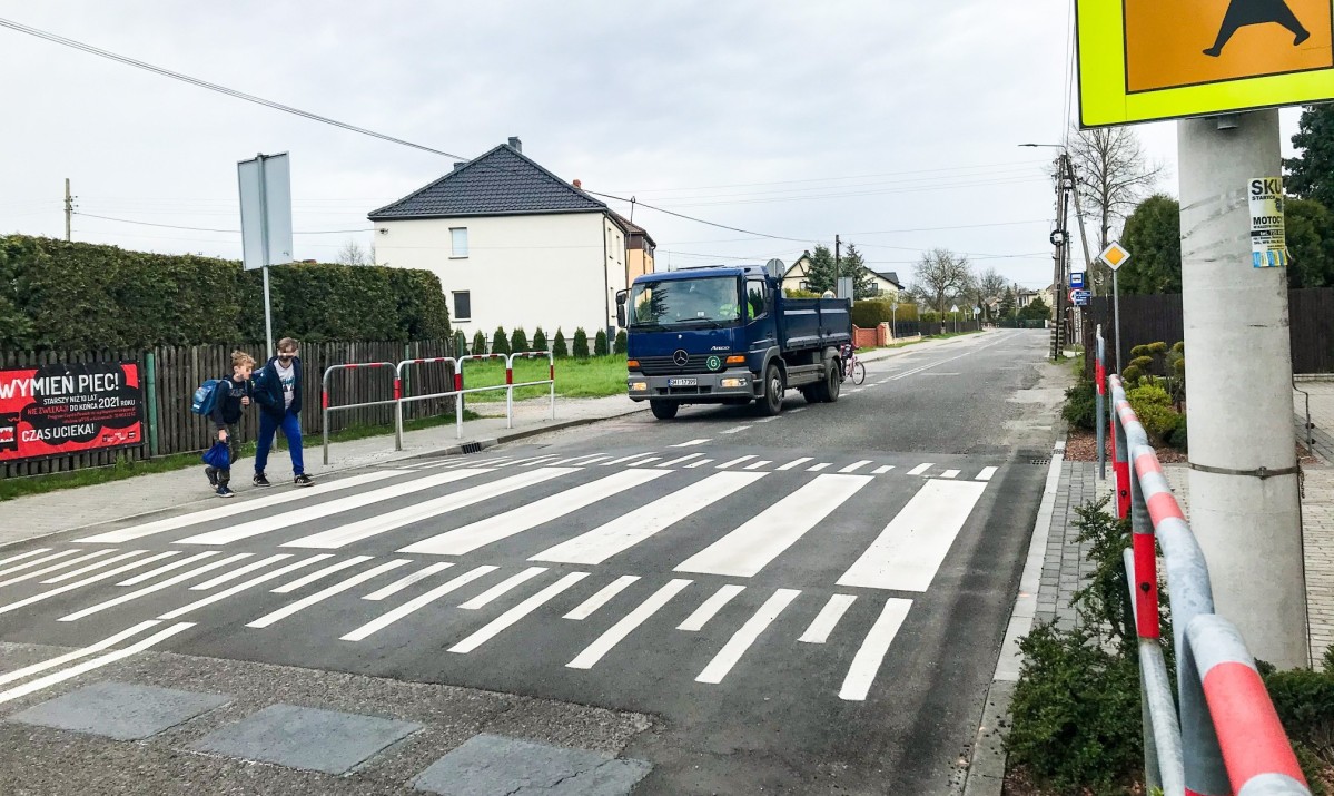 Na ul. Św. Jana Pawła II w Studzienicach przy szkole powstało wyniesione przejscie dla pieszych. Przechodzi przez nie dwójka uczniów. Przed nim stoi samochod ciężarowy.