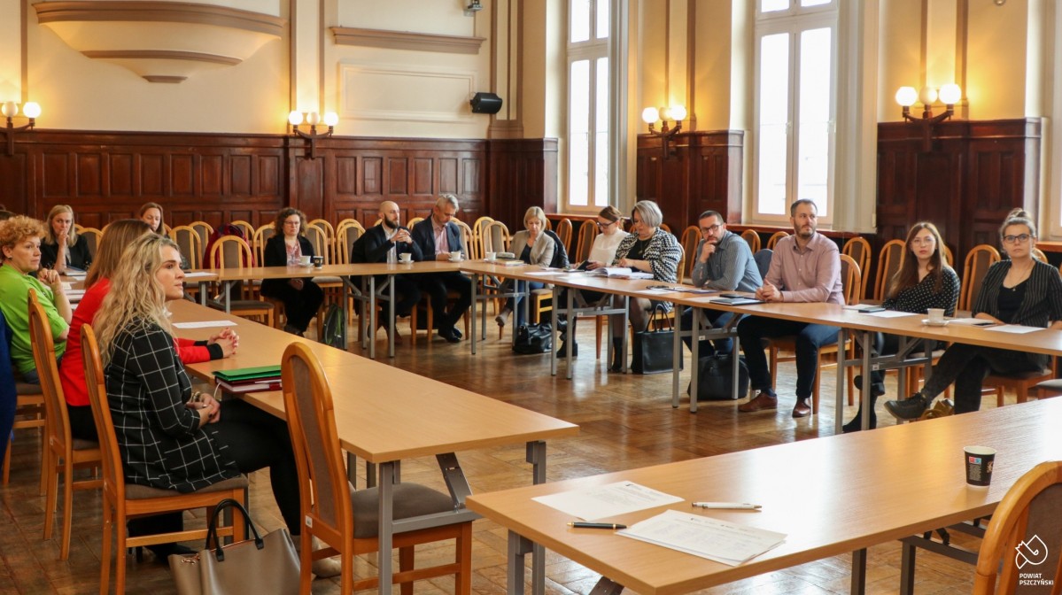 Uczestnicy spotkania siedzą przy stołach w sali sesyjnej.