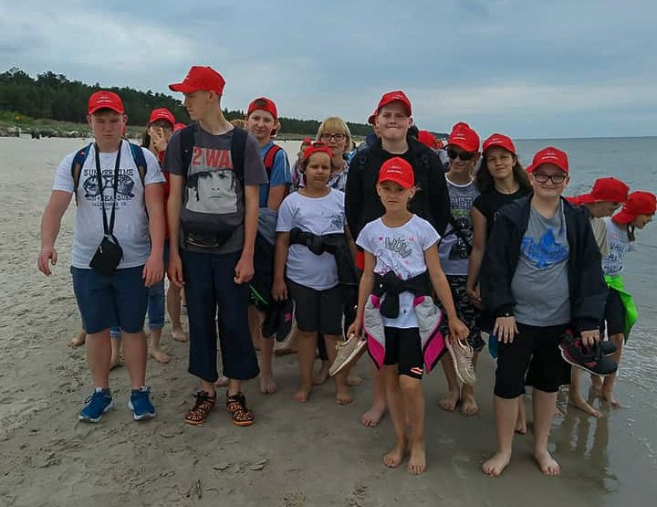 Uczniowie stojący na plaży, za ich plecami morze bałtyckie.