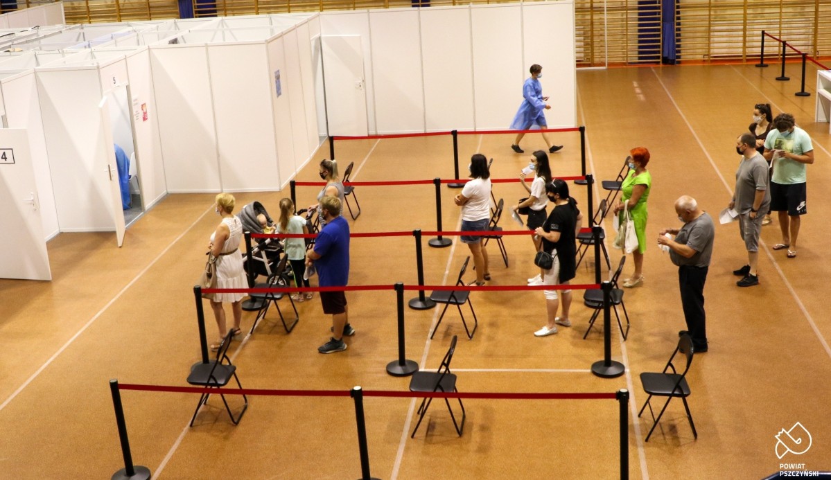 punkt szczepień zlokalizowany jest w hali sportowej. Przed białymi boksami stoją ludzie w kolejce.