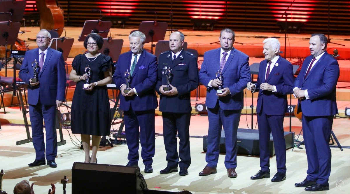 Na scenie sali koncertowej stoją wyróznieni starostowie razem z prof. Jerzym Buzkiem oraz marszałkiem