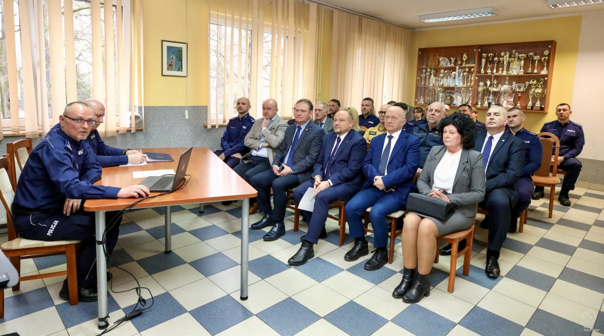 Zaproszeni goście na krzesłach w pomieszczeniu, gdzie przy stole siedzą komendanci.
