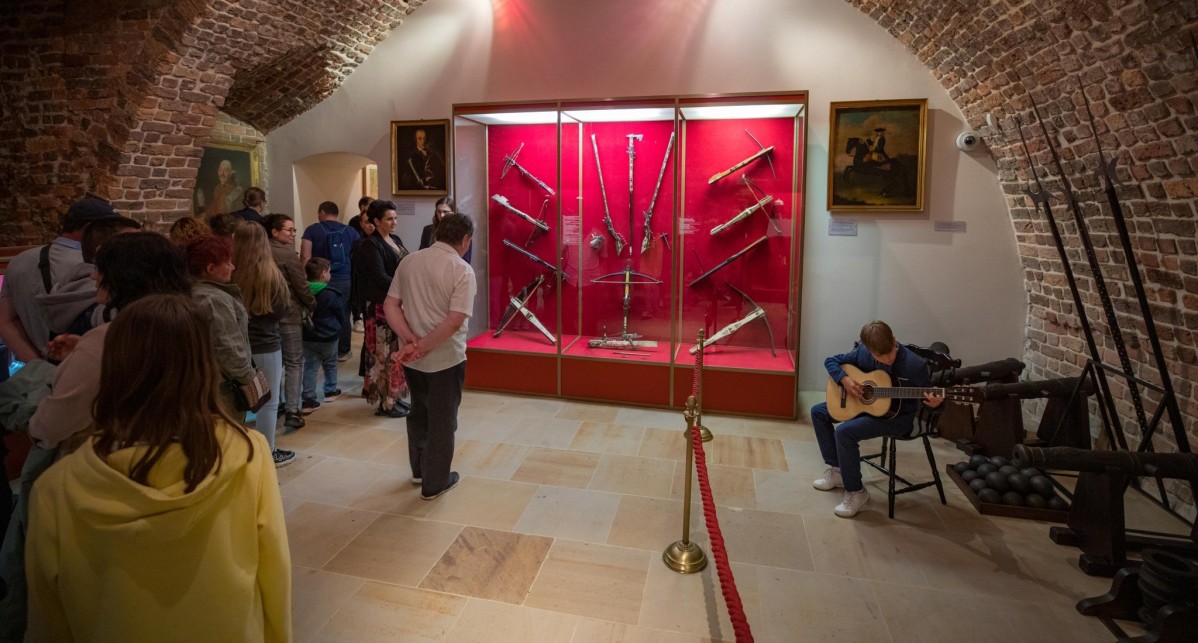 Wystawa zbrojownia we wnetrzach muzeum zamkowego w Pszczynie podczas Nocy Muzeów. Wielu zwiedzających, młody chłopak gra na gitarze