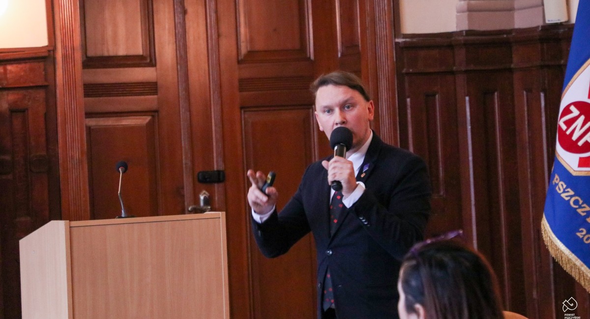 Mirosław Kozik stoi w sali sesyjnej i przemawia do mikrofonu