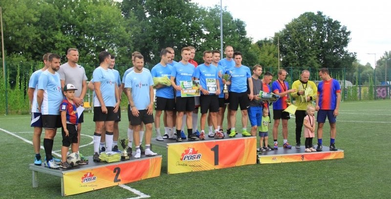 Na podmium ustawionym na boisku piłkarskim stoją trzy drużyny - laureaci Turnieju o Puchar Starosty