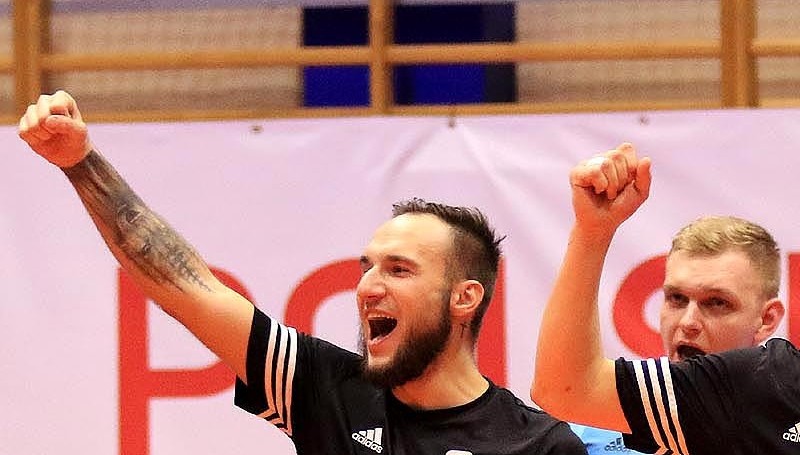 Zawodnocy futsalowej druzyny NEXX Goczałkowice, ubrani w czarne stroje, unoszą ręce w geścoie zwycięstwa.