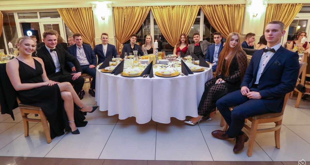 Ubrani elegancko uczestnicy studniówki siedza za okrągłym stołem w restauracji i pozują do zdjęcia