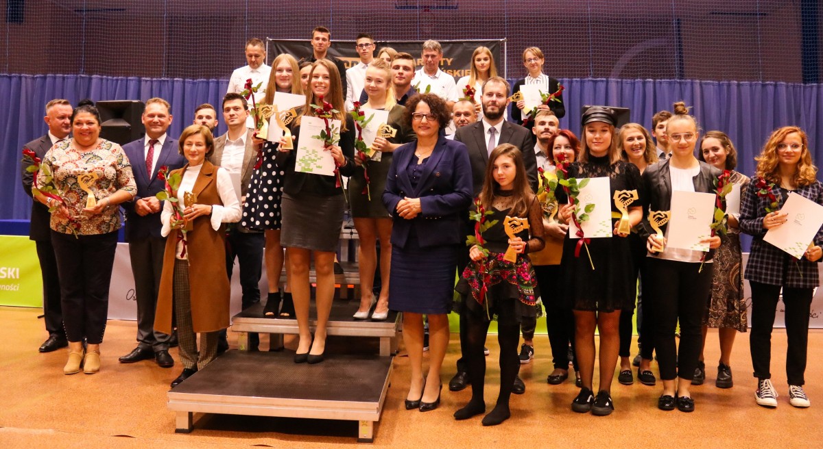 Stojący na podium laureaci nagród starosty w dziedzinie sportu. Hala sportowa.