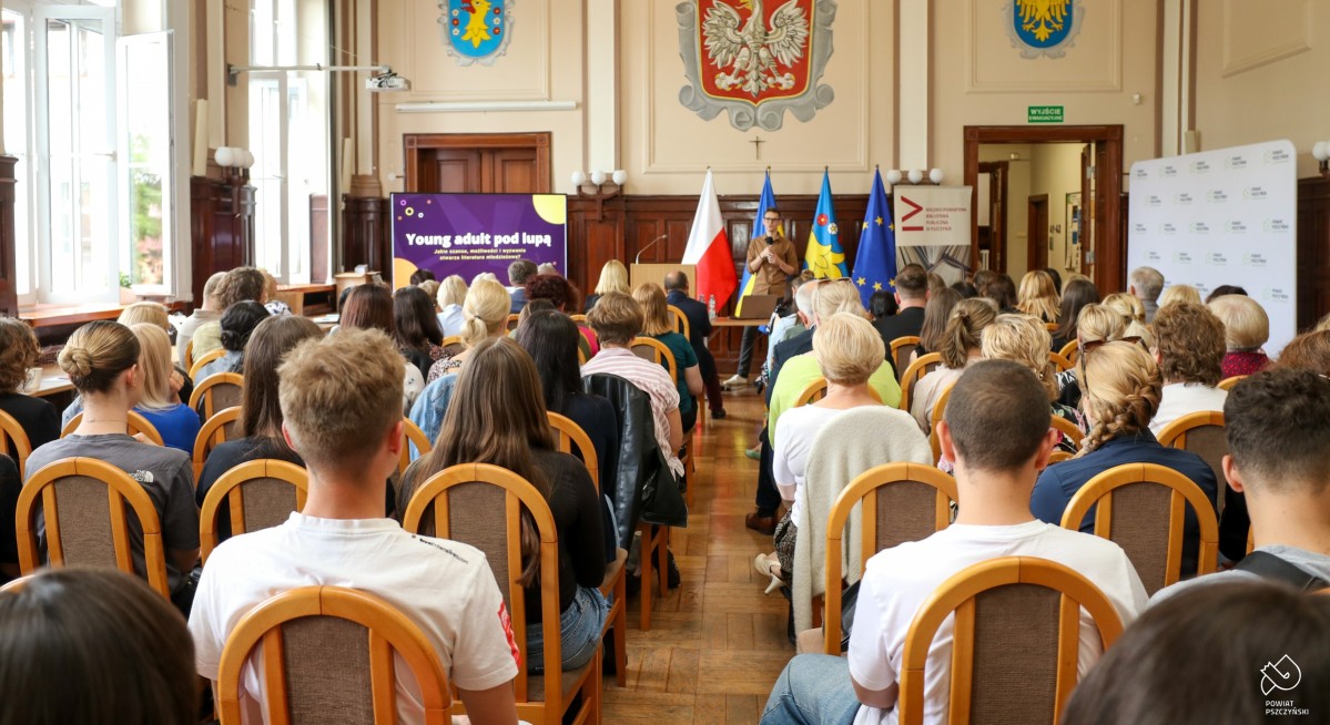 Uczestnicy siedzą w wypełnionej sali sesyjnej.