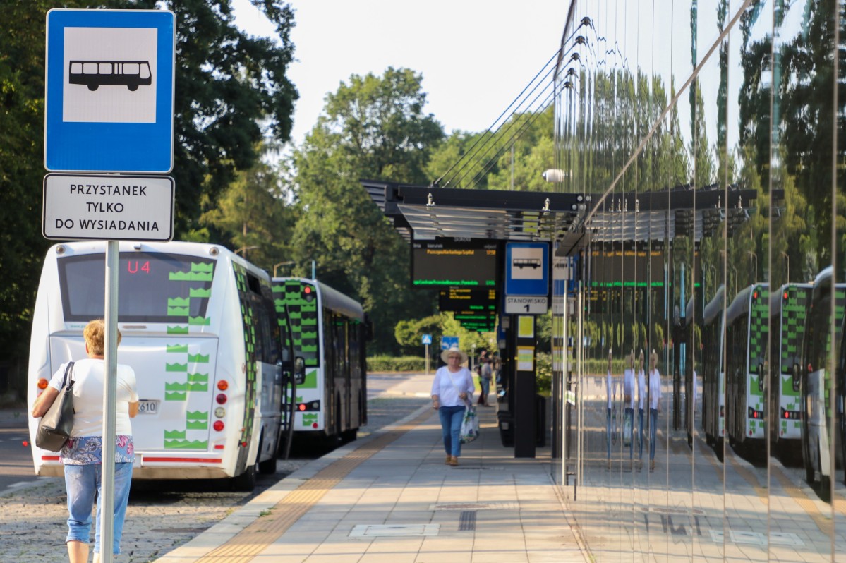 Budynek centrum przesiadkowego, przy wiatach autobusowych stoi komunikacja powiatowa. Przechodzą pasażerowie.