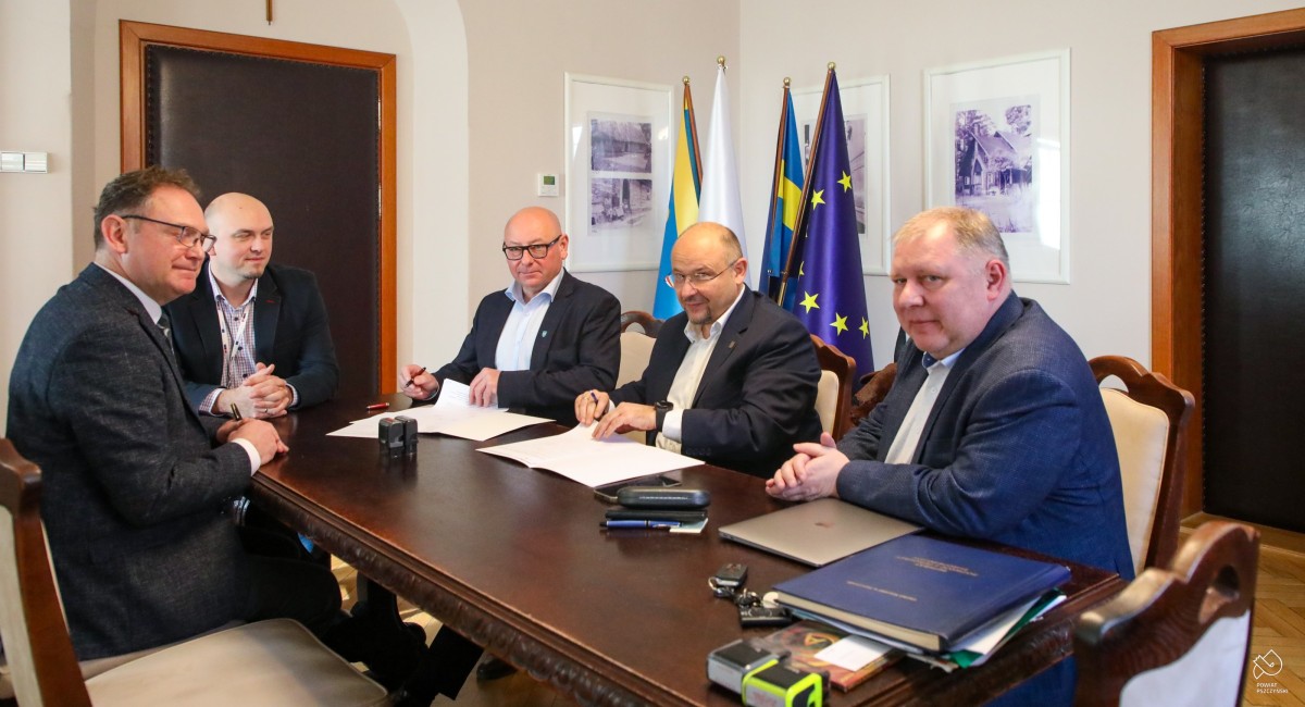 Za stołem w gabinecie gurmistrza siedzi burmistrz, starosta, wicestarosta, skarbnik i kierownik referatu. Podpisują dokumenty