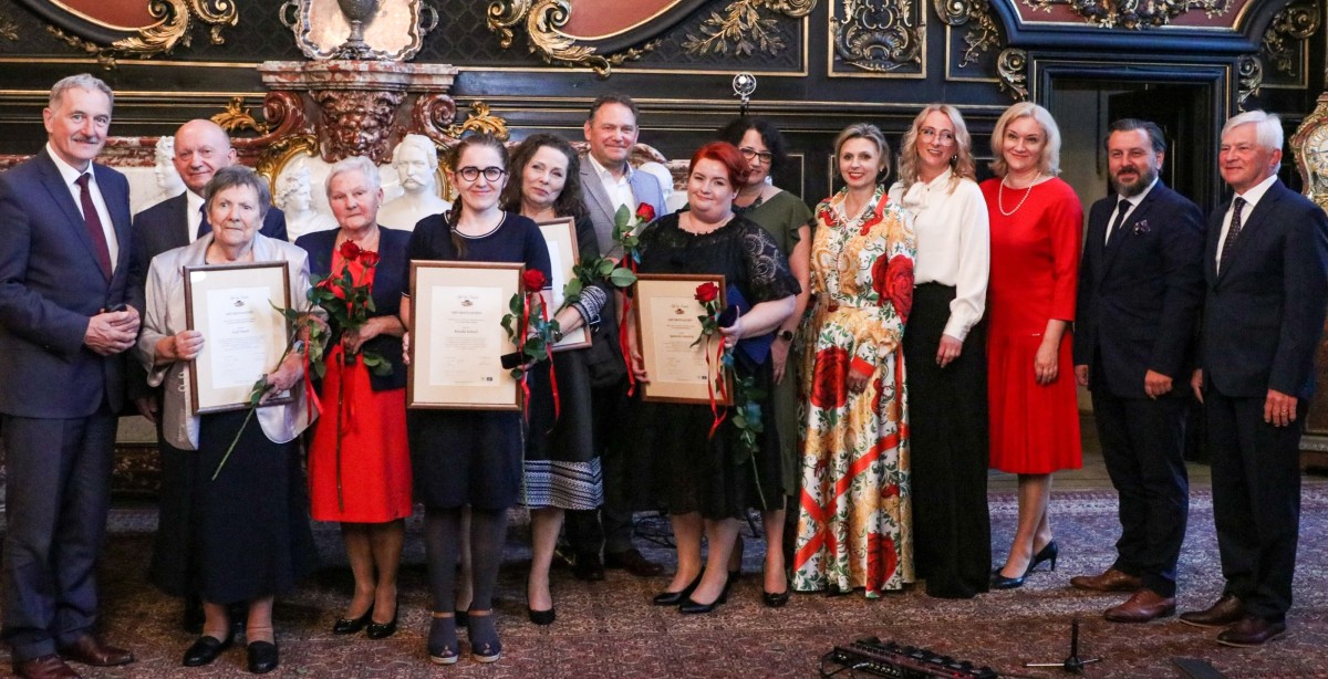 Wyróżnione kobiety z samorządowcami i członkami kapituły we wspólnym zdjęciu w sali lustrzanej zamku pszczyńskiego.