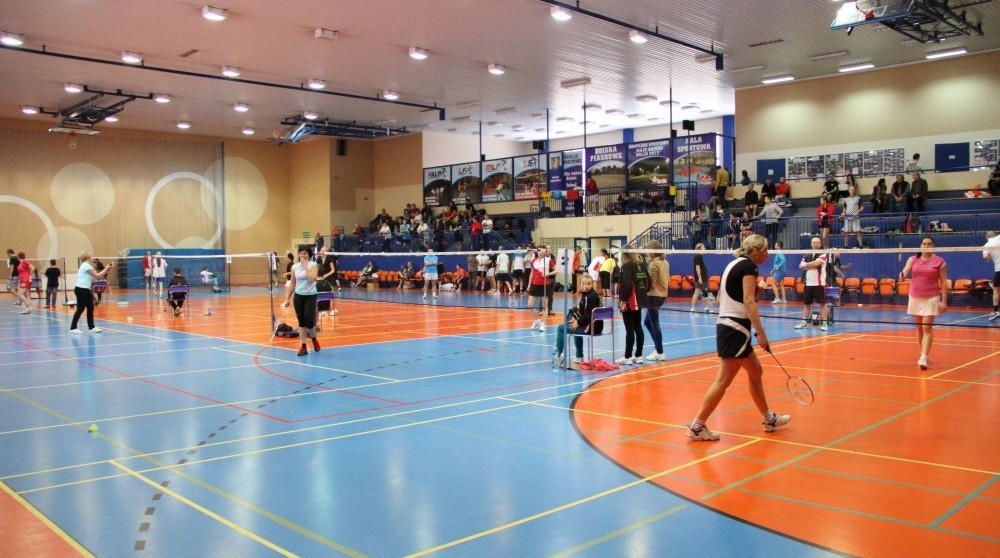 Na parkiecie hali sportowej trwa równoczesnie kilka meczów badmintona. W tyle widać trybuny.