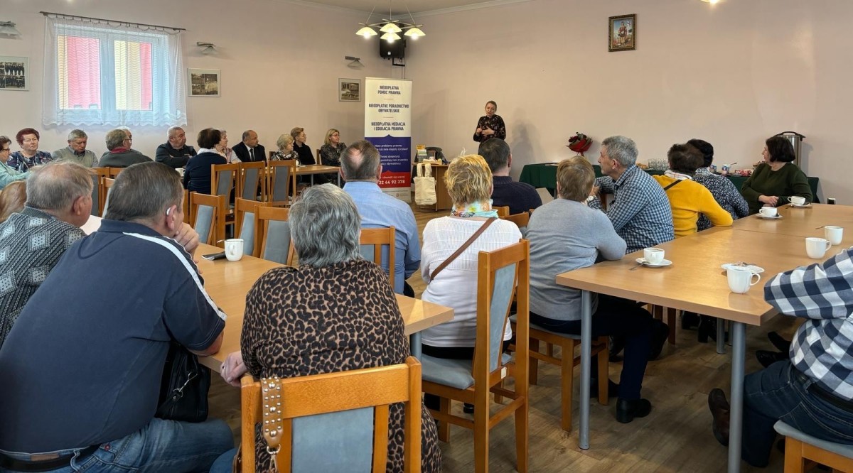 Trwa wykład, uczestnicy siedzą przy stołach, przemawia prawniczka.