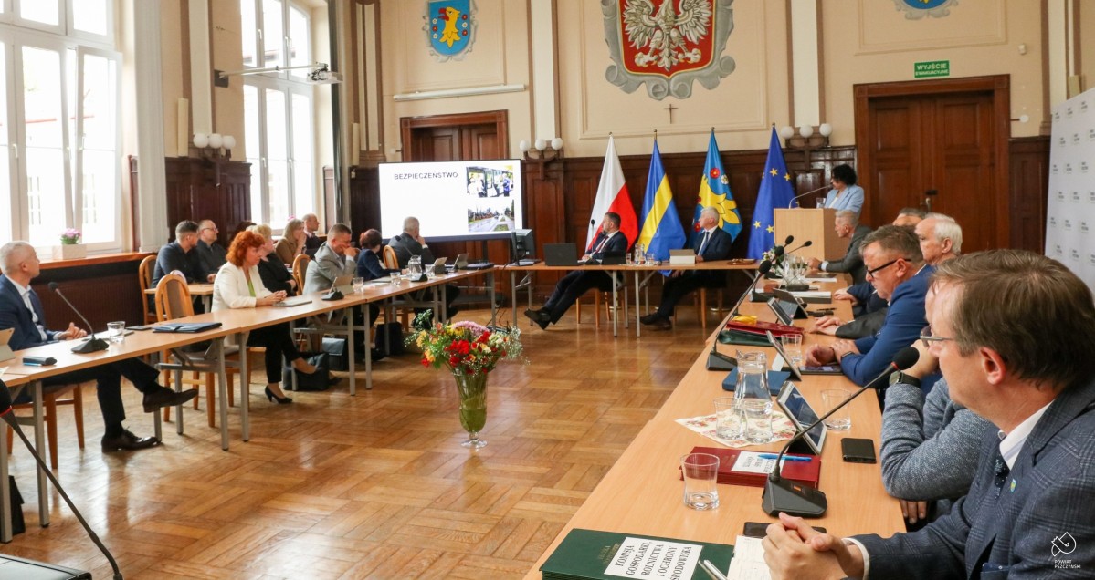 W sali sesyjnej trwa sesja rady powiatu. Radni siedzą za stołami ułozonymi w kształt kwadratu