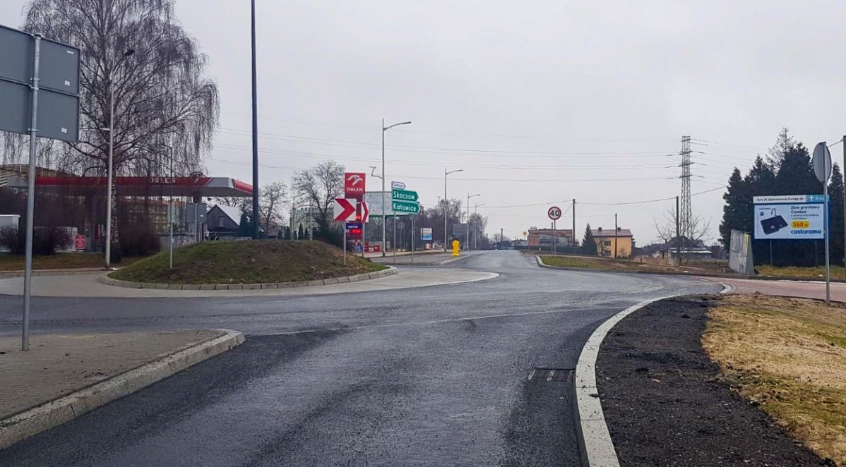 Przebudowana droga na rondo. Nawierzchnia jedni jest mokra. Pada deszcz.
