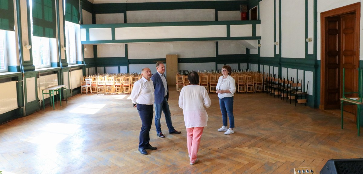Przedstawiciele zarządu powiatu oraz dyrektor szkoły stoja w pustej auli liceum