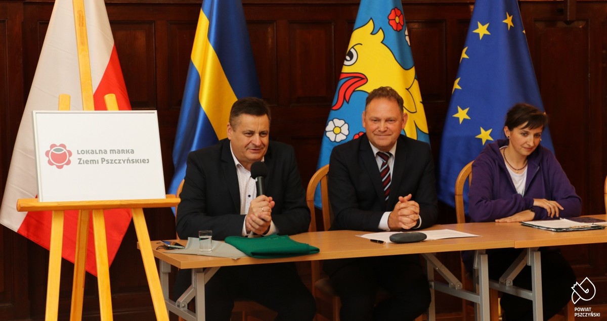 Za stołem w sali sesyjnej siedzą wicestarosta, prezes towrayzstwa miłosników ziemi psczzyńksiej i lokalna producentka.