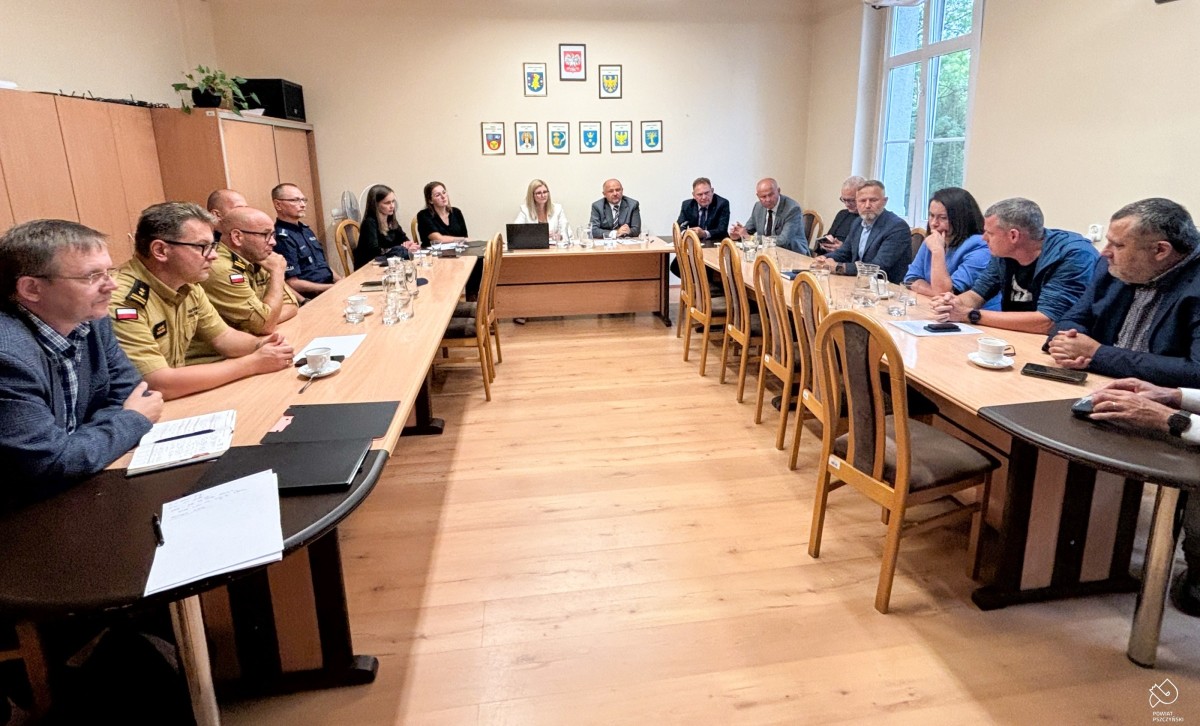 W pomieszczeniu za stołami siedzą przedstawiciele służb