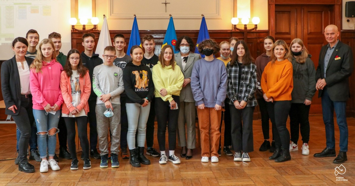 Gryupa uczniów z nauczycielkami, starosta i sekretarzem w sali sesyjnej starostwa