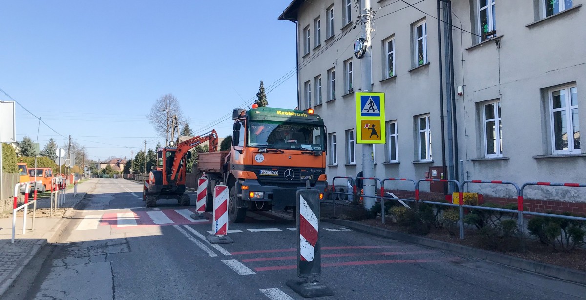 W Studzieniach przy szkole podstawowej trwa budowa wyniesionego przejścia dla pieszych. Na drodze stoi koparka i robotnicy.