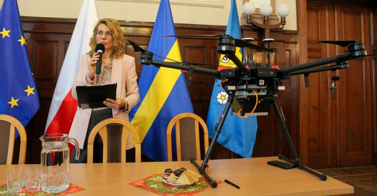 Prezes Stowarzyszenia nie dokarmiaj smoga mówi przez mikrofon, na stole stoi dron.