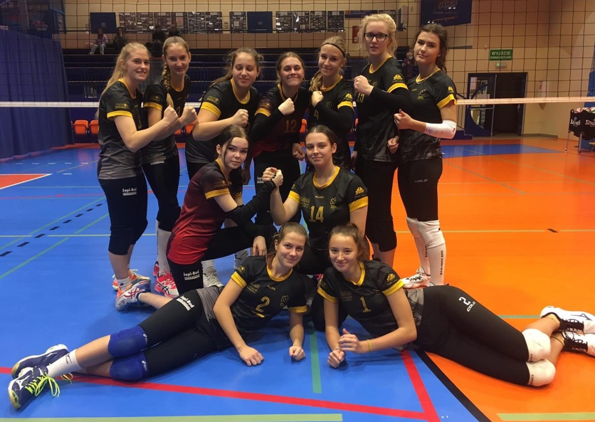 Siatkarska drużyna na zdjęciu grupowym w hali sportowej, w tle siatka.