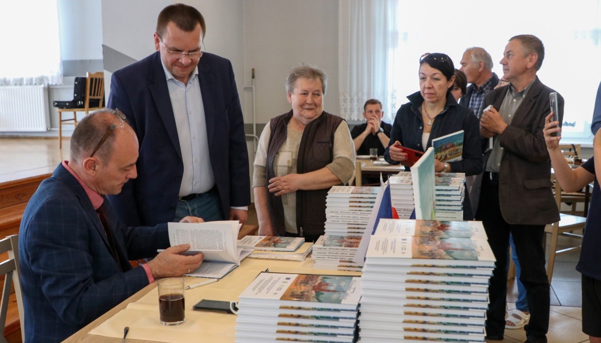 Grzegorz Sztoler siedząc za stołem podpisuje swoją książkę. Ustawiła się kolejka chętnych po wpis.