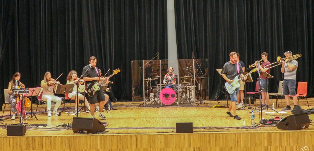 Na scenie pszczyńskiego centrum kultury stoją muzycy - grają na perkusji, gitarach, instrumentach smyczkowych i dętych