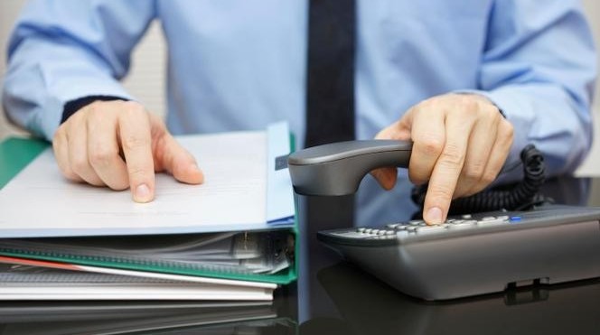 Dłonie trzymające słuchawkę, wybierające numer telefonu. Druga dłoń położona na dokumentach.
