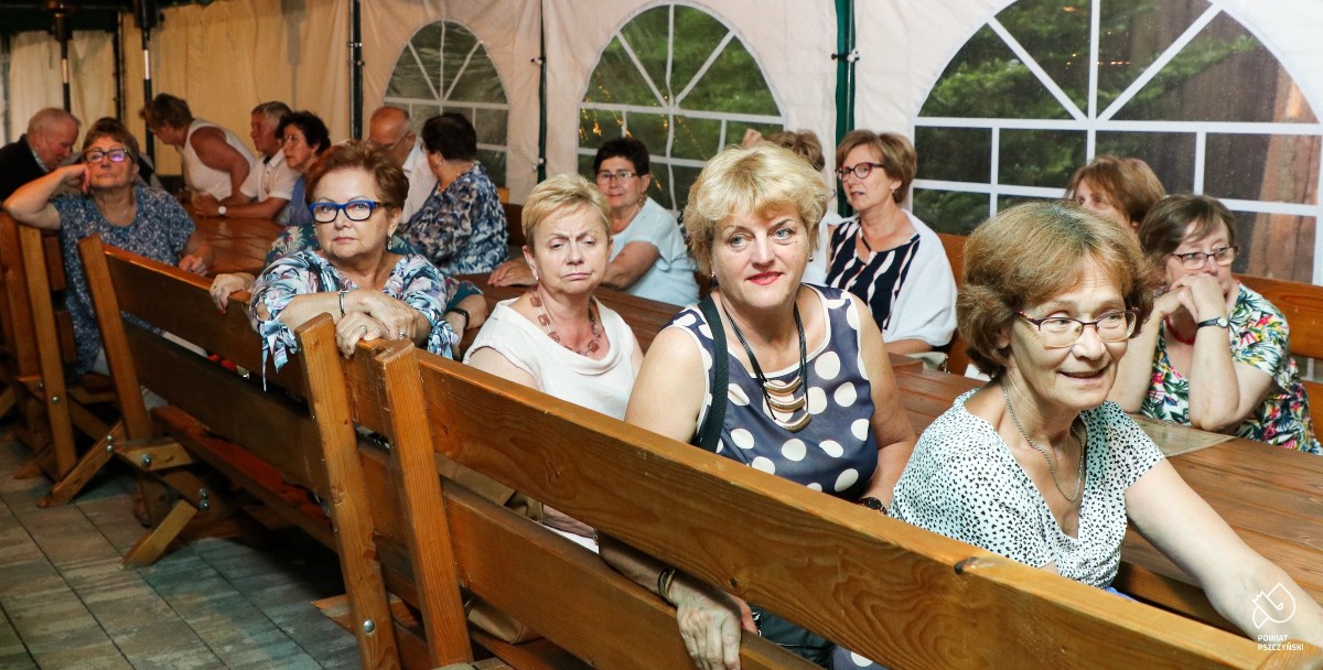Uczestniczki zajeć UTW siedzące pod namiotem za drewnianym stołem.