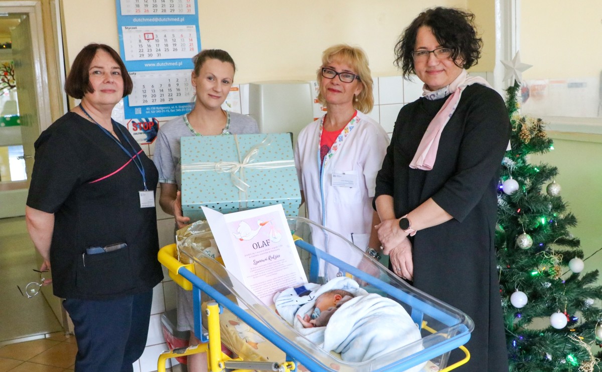W przeźroczystym szpitalnym łóżeczku śpi mały Olaf, obok niego stoją mama, starosta, lekarka i pielęgniarka