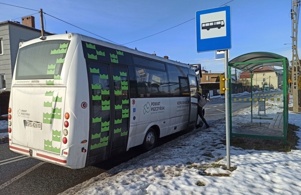 Biały autobus z zielonymi elementami graficznymi stoi przy przystanku. Na poboczu śnieg.
