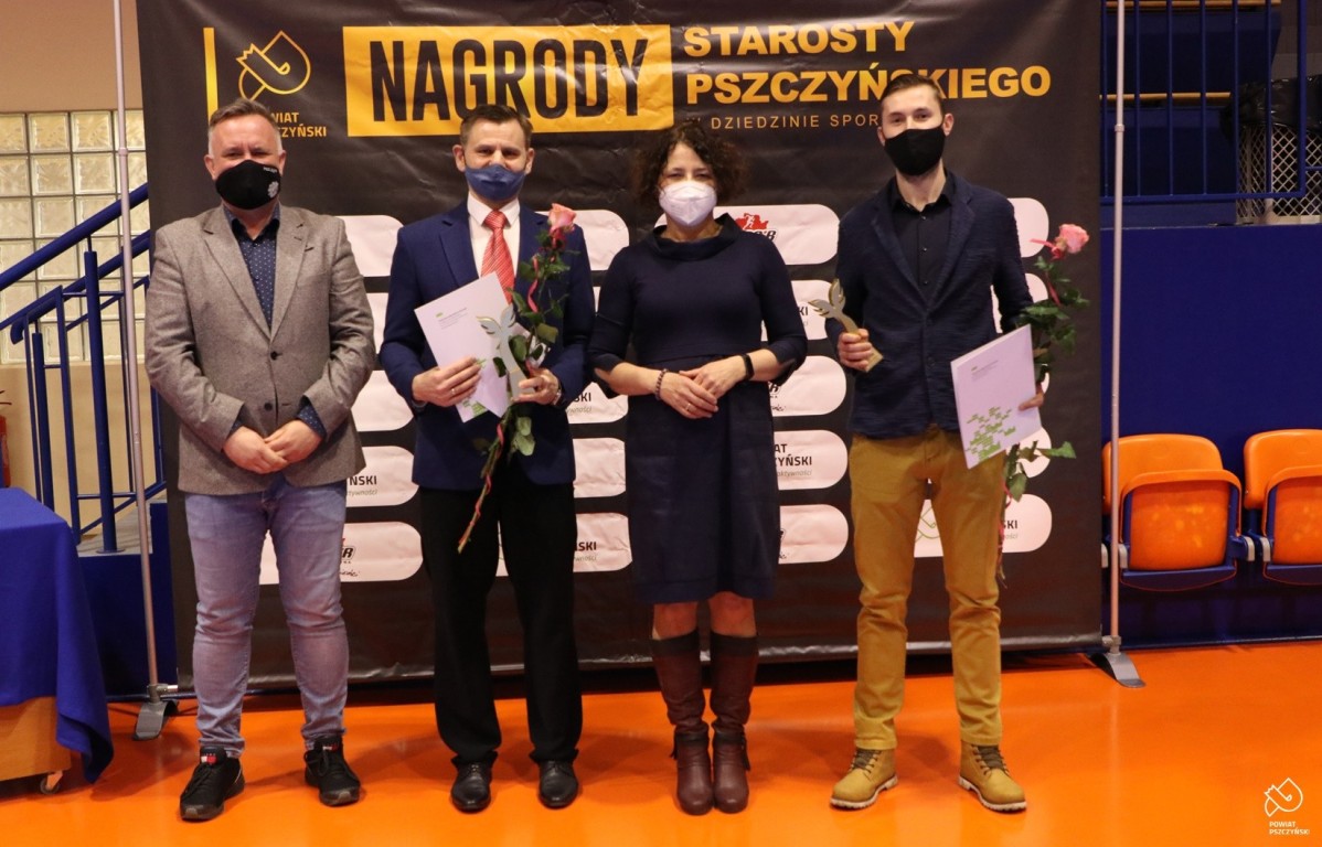 Starosta, wicestarosta i dwóch mężczyzn na tle czarnej ścianki z napisem Nagrody Starosty Pszczyńskiego w dziedzinie sportu.