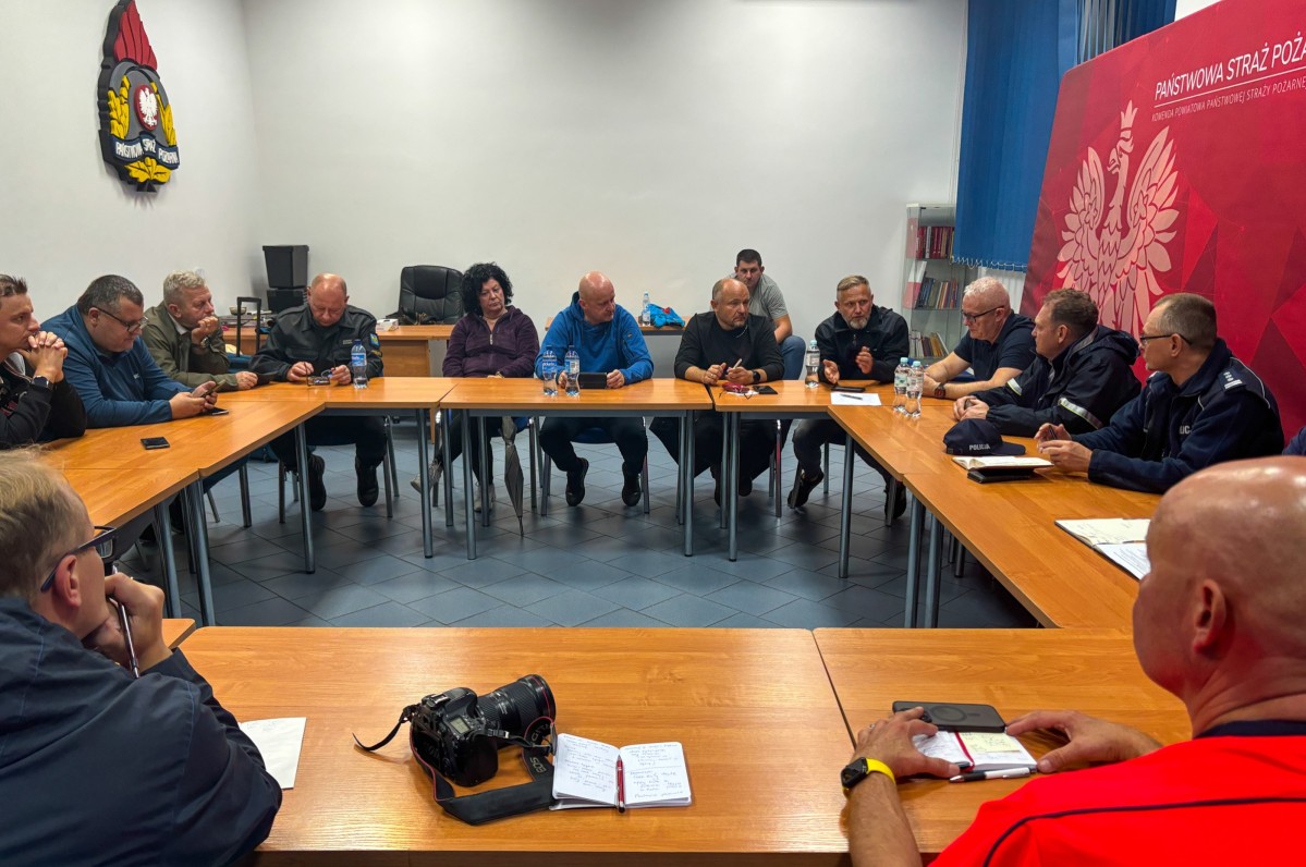 Przedstawiciele służb i jednostek siedzą za stołem w kształcie kwadratu