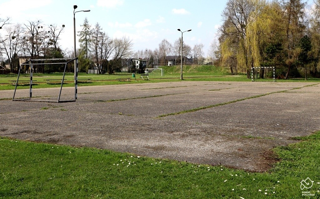 Asfaltowe boisko ze zniszczoną nawierzchnią z dwoma bramkami.