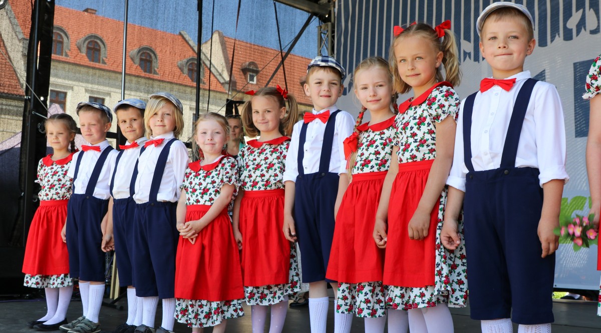 Dzieci ubranme w stroje regionalne stoja na scenie i uśmiechają się
